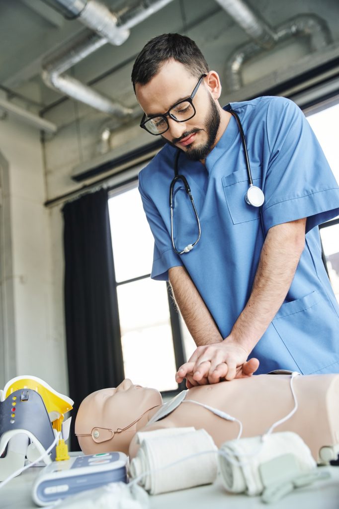 bearded professional paramedic in eyeglasses and blue uniform practicing chest compressions on CPR